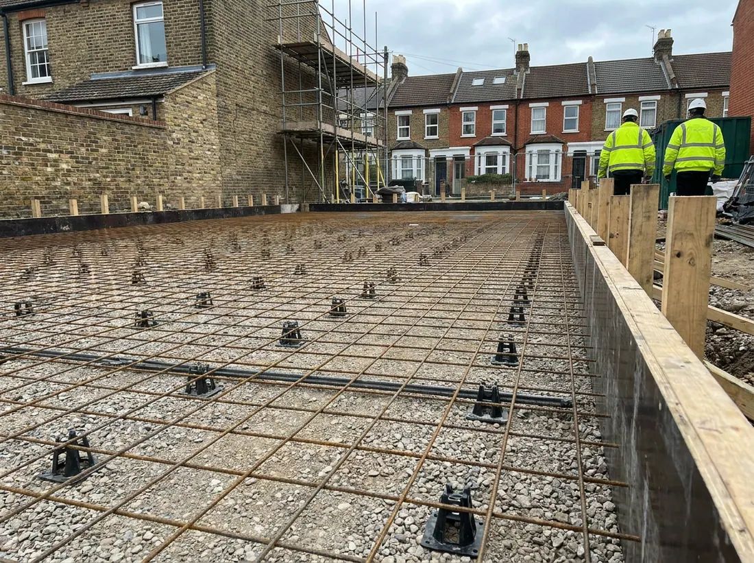 A mini excavator digging foundation trenches beside a house